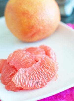 peeled grapefruit segments on a white plate with a whole grapefruit in the background