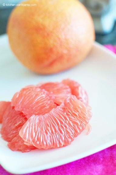 peeled grapefruit segments on a white plate with a whole grapefruit in the background