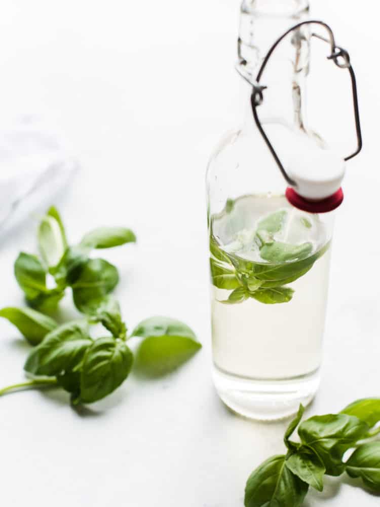 Fresh basil leaves in a glass bottle of simple syrup to make Cherry Basil Sorbet