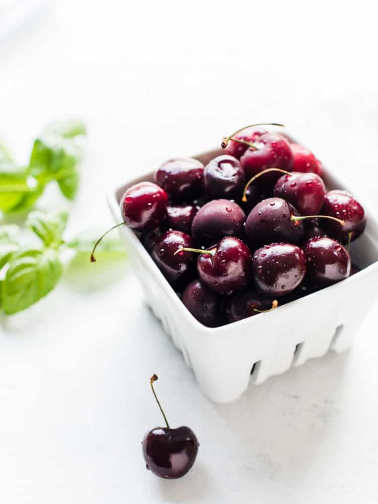 Fresh cherries in a white ceramic box with basil leaves in the background to make Cherry Basil Sorbet