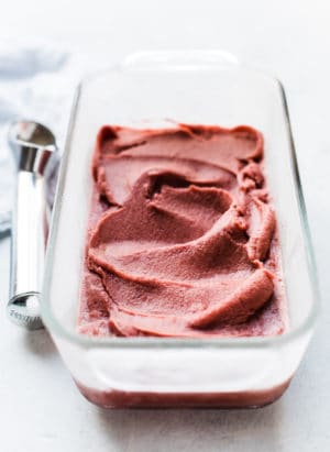 Cherry Basil Sorbet in a glass loaf pan with an ice cream scoop.