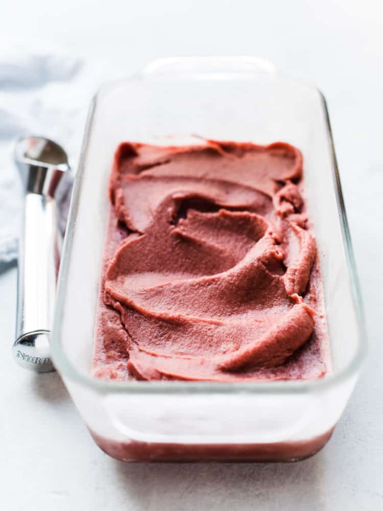 A glass loaf pan of Cherry Basil Sorbet with an ice cream scoop