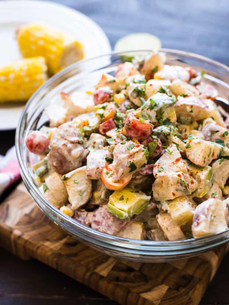 Southwestern Potato Salad in a glass bowl on a wooden board with corn on the cob in the background.