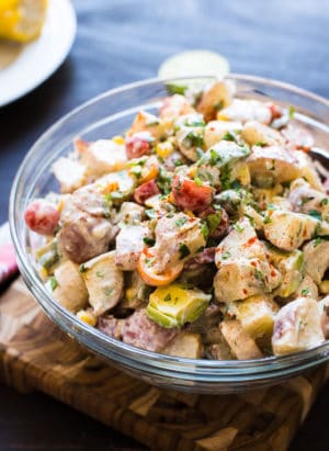 Southwestern Potato Salad in a glass bowl with potatoes, tomatoes, avocado, and corn.