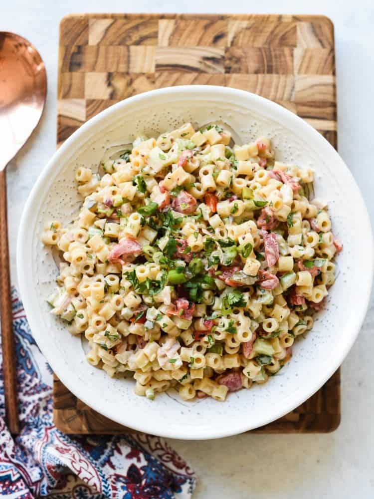 Fireworks Pasta Salad in a white bowl on a wooden cutting board