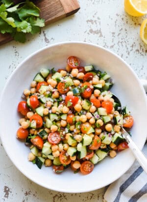 Chickpea salad with tomatoes and cucumbers in a glass bowl on a rustic white background