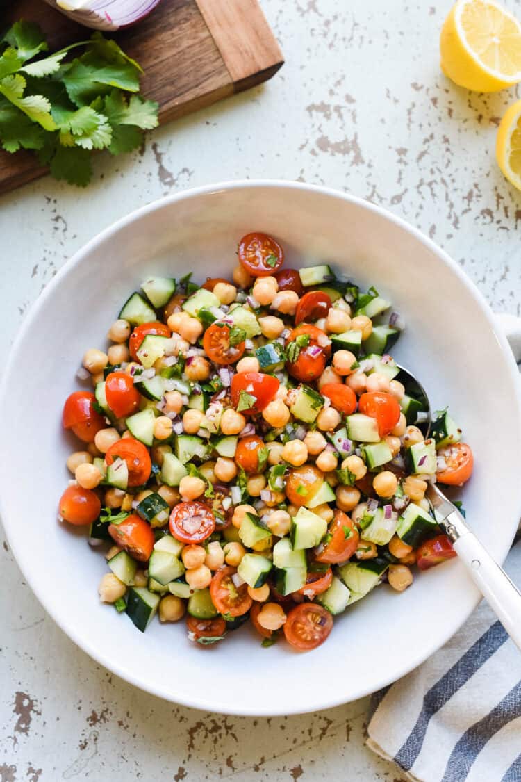 Chickpea salad with tomatoes and cucumbers in a glass bowl on a rustic white background