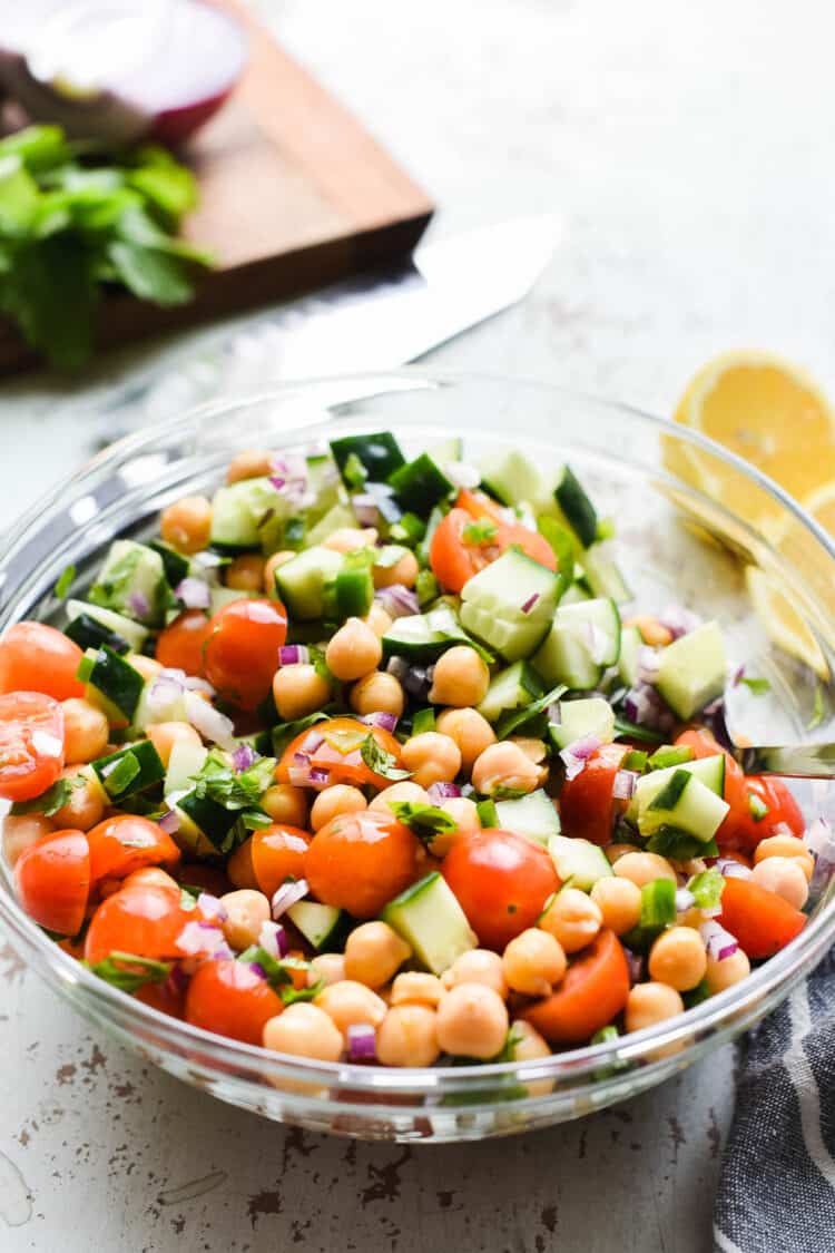 chick pea salad with tomatoes and cucumbers in a glass bowl on a rustic white background