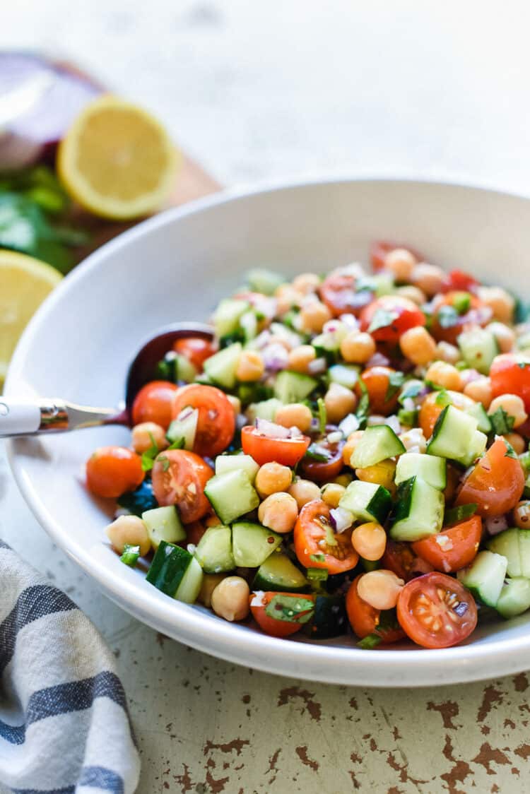 Chickpea salad with garbanzo beans, cherry tomatoes, cucumbers, red onions, cilantro, and a delicious dressing in a white bowl.