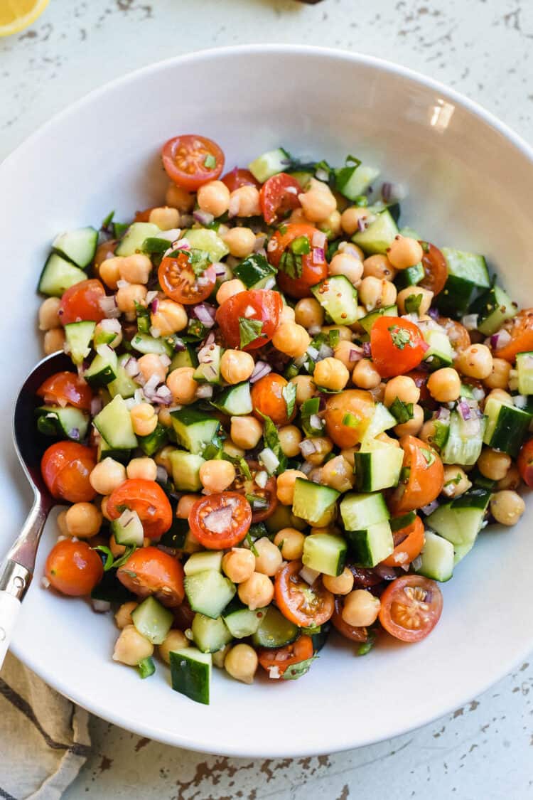 chick pea salad with tomatoes and cucumbers in a white bowl on a rustic white background