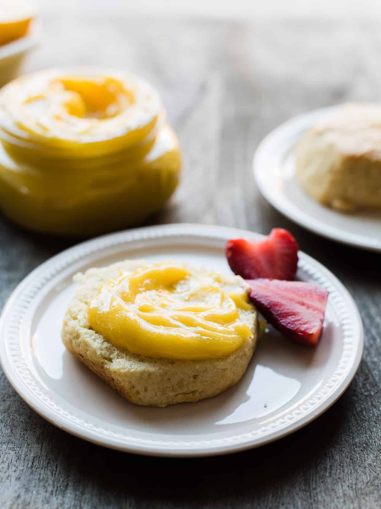 Lemon curd on scone with fresh berries on a plate.