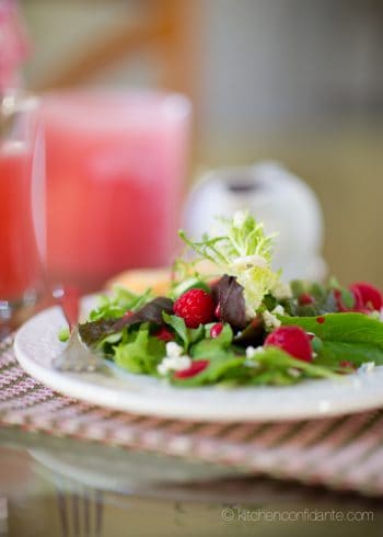 A plate of green salad topped with raspberries, cheese, and homemade raspberry salad dressing.