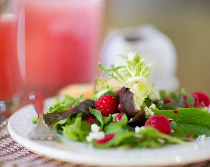 A plate of green salad topped with raspberries, cheese, and homemade raspberry salad dressing.