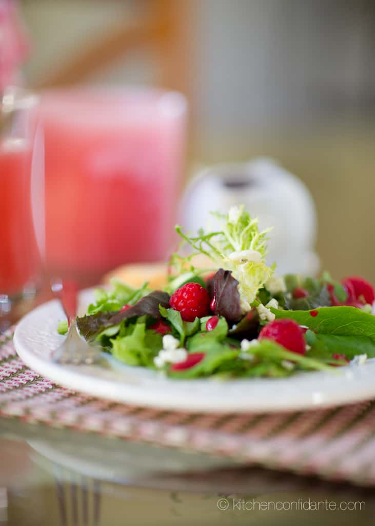 A plate of green salad topped with fresh raspberries and raspberry salad dressing made with frozen raspberries.