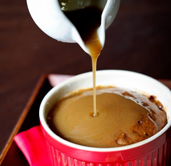 A red ramekin filled with a fresh fig cake. A small white pitcher pours toffee sauce over the top, finishing up the Sticky Toffee Pudding Cake with Figs