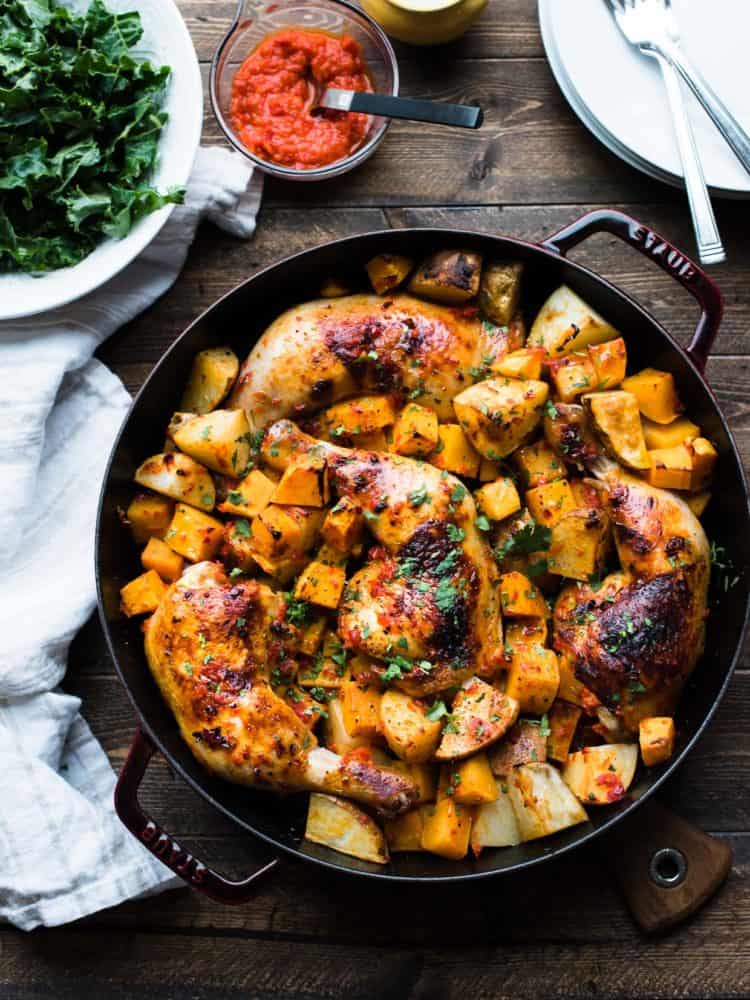Harissa-style Roast Chicken with Butternut Squash and Potatoes served in a Dutch oven on a wooden counter top.