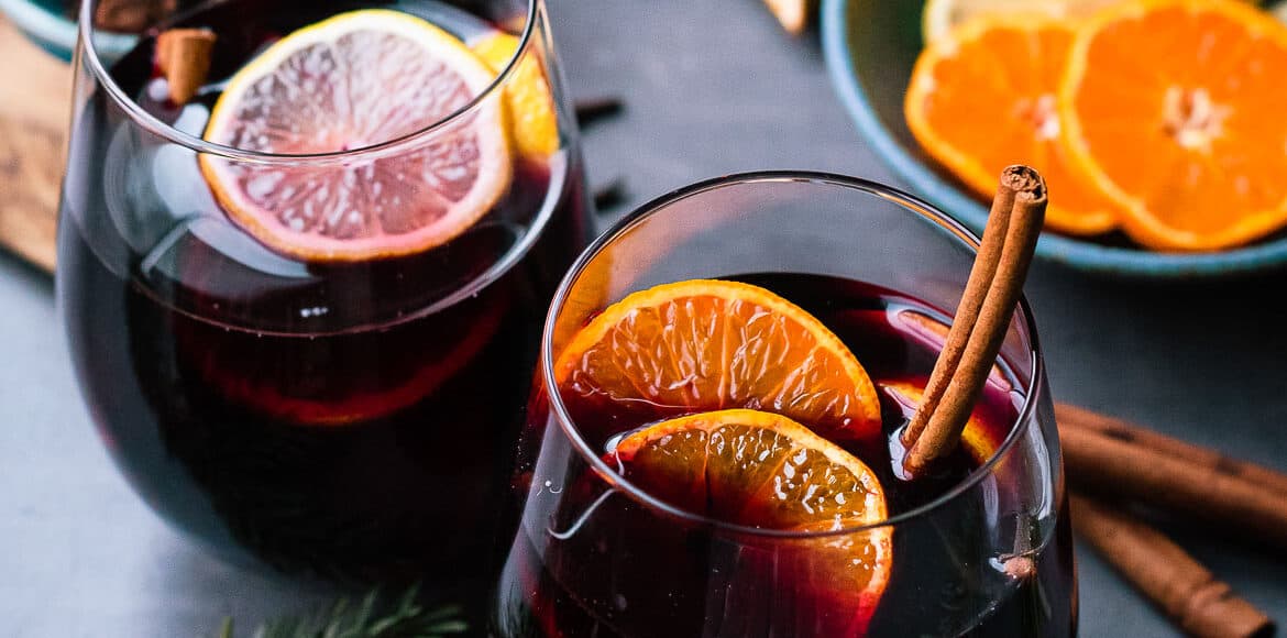 Glasses of mulled wine with citrus, cinnamon, cloves and more spices.