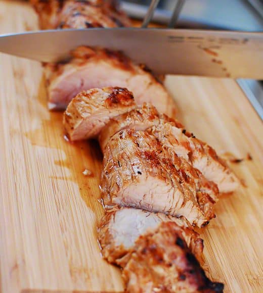 Sliced pork tenderloin on cutting board being cut with a knife