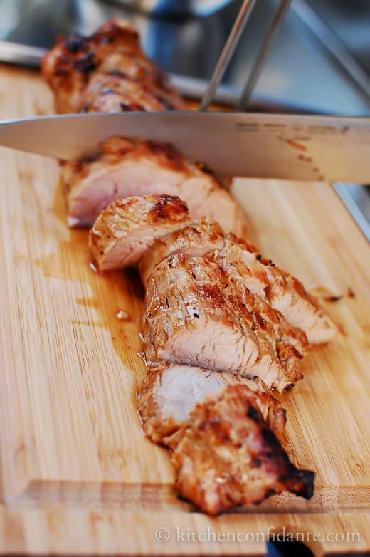 Sliced pork tenderloin on cutting board being cut with a knife