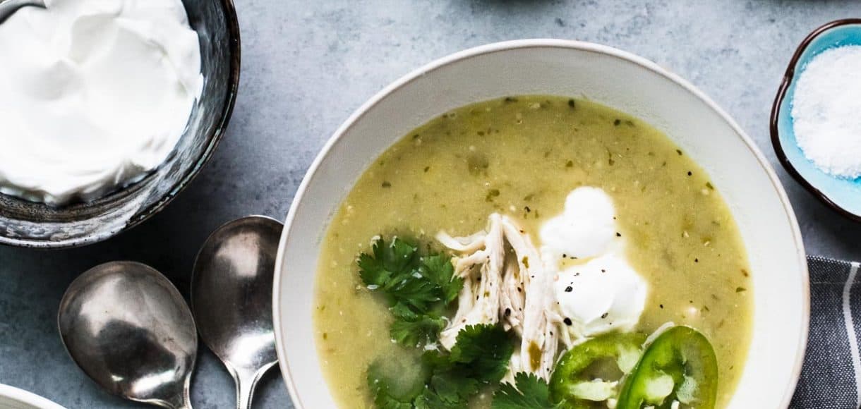 A bowl of Roasted Tomatillo Chicken Soup garnished with cilantro, jalapeno, and creme fraiche.