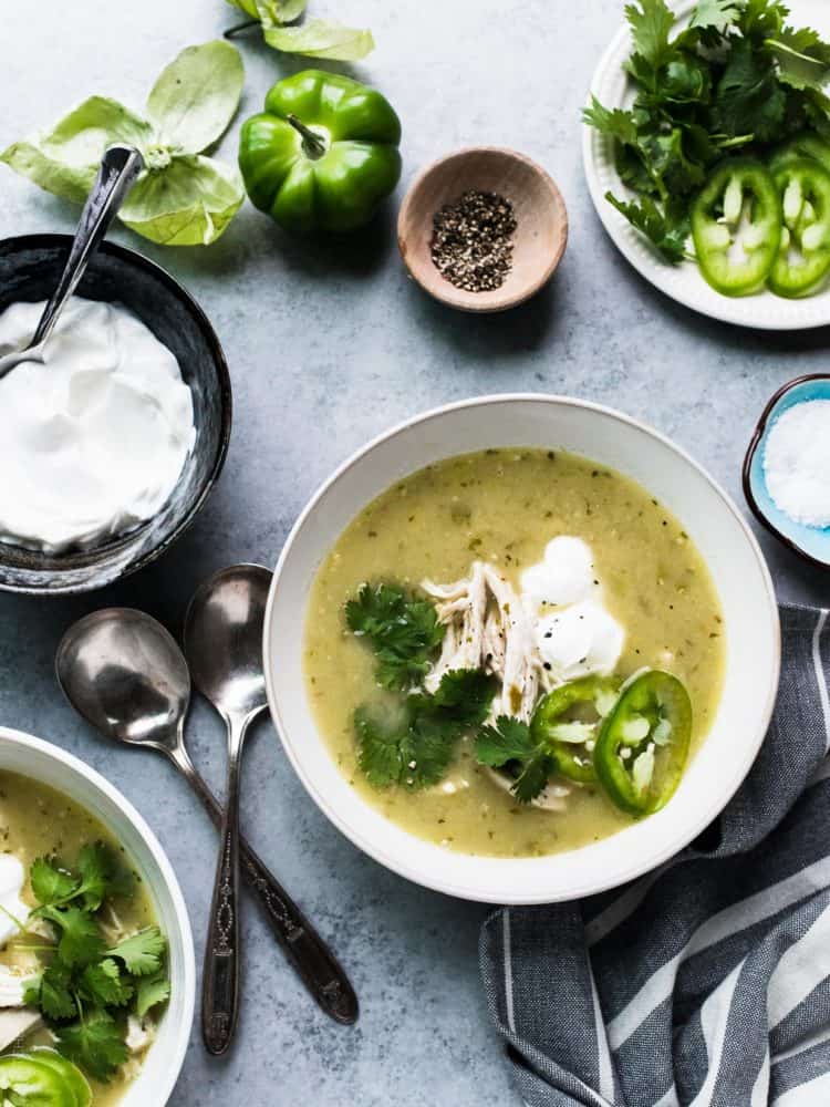 A bowl of Roasted Tomatillo Chicken Soup garnished with cilantro, jalapeno, and creme fraiche.
