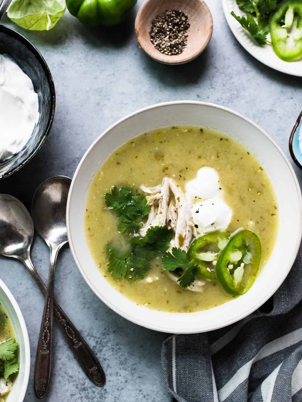 A bowl of Roasted Tomatillo Chicken Soup garnished with cilantro, jalapeno, and creme fraiche.