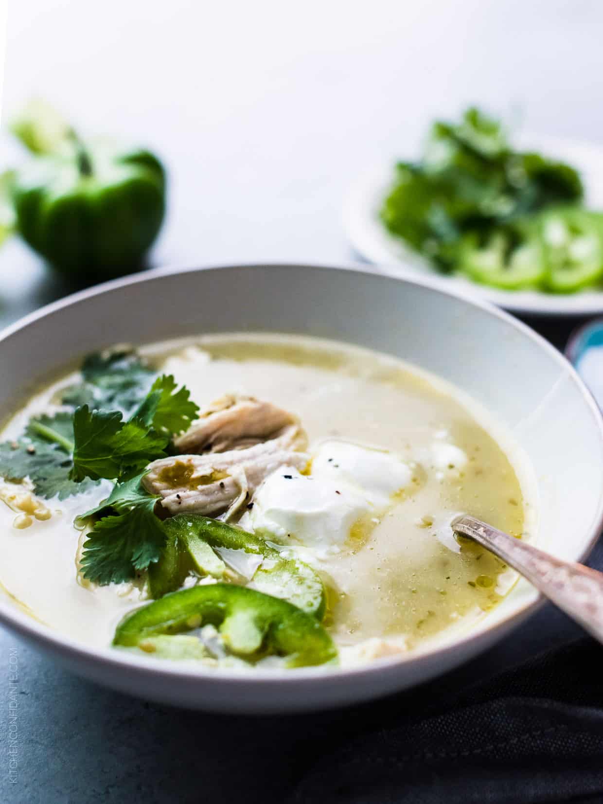 A bowl of Roasted Tomatillo Chicken Soup garnished with cilantro, jalapeno, and creme fraiche.