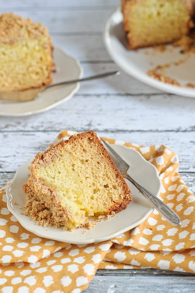 A white plate with a slice of meyer lemon coffee cake laying on it.