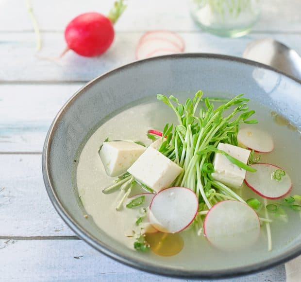 A bowl of fresh tofu soup with pea shoots and radishes floating on top.