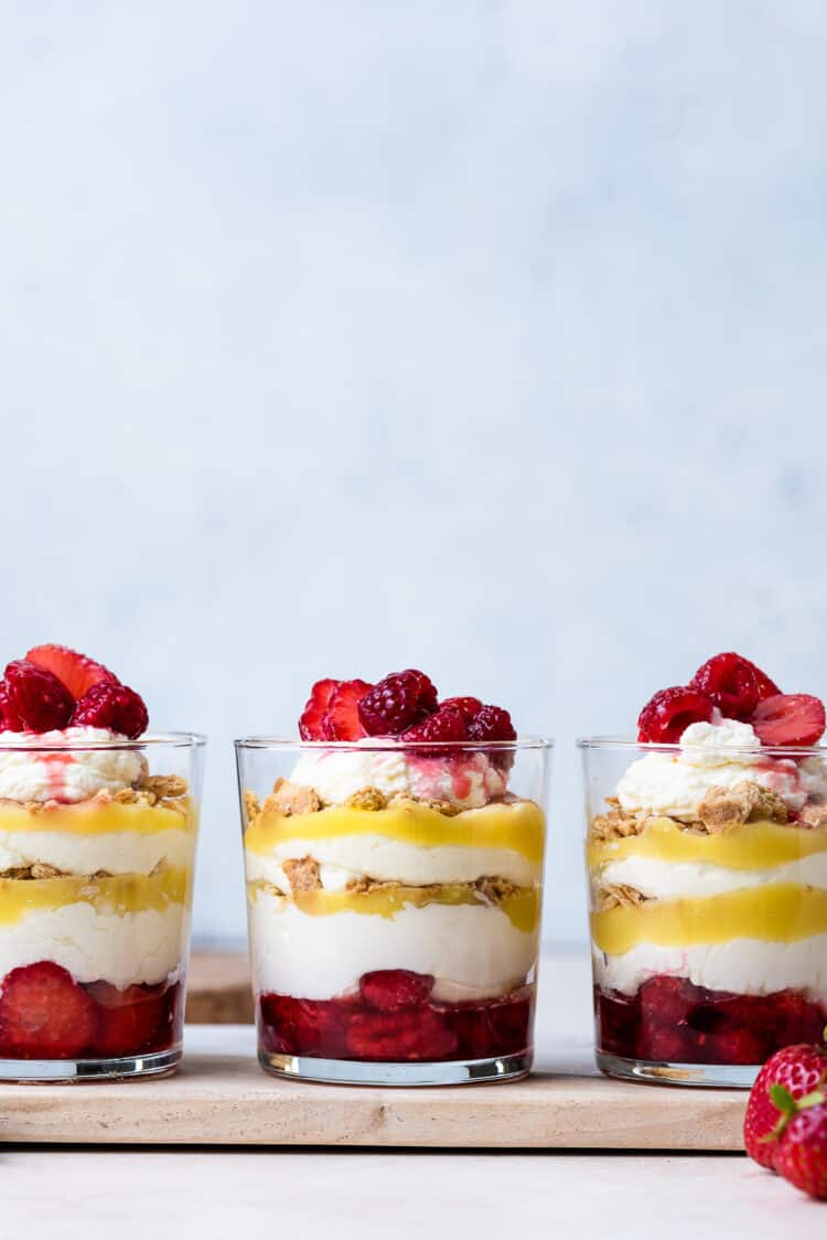 Glass cups of Lemon-Berry Cheesecake Parfaits with lemon curd and topped with berries.