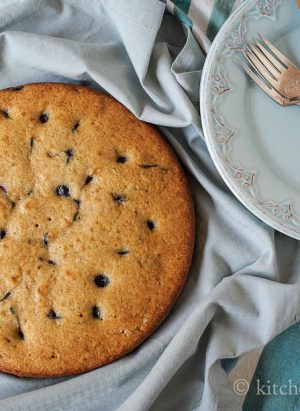 A round blueberry buttermilk cake with plate, fork, and knife.