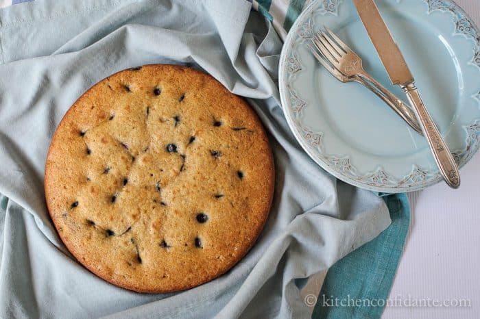 A round blueberry buttermilk cake with plate, fork, and knife.