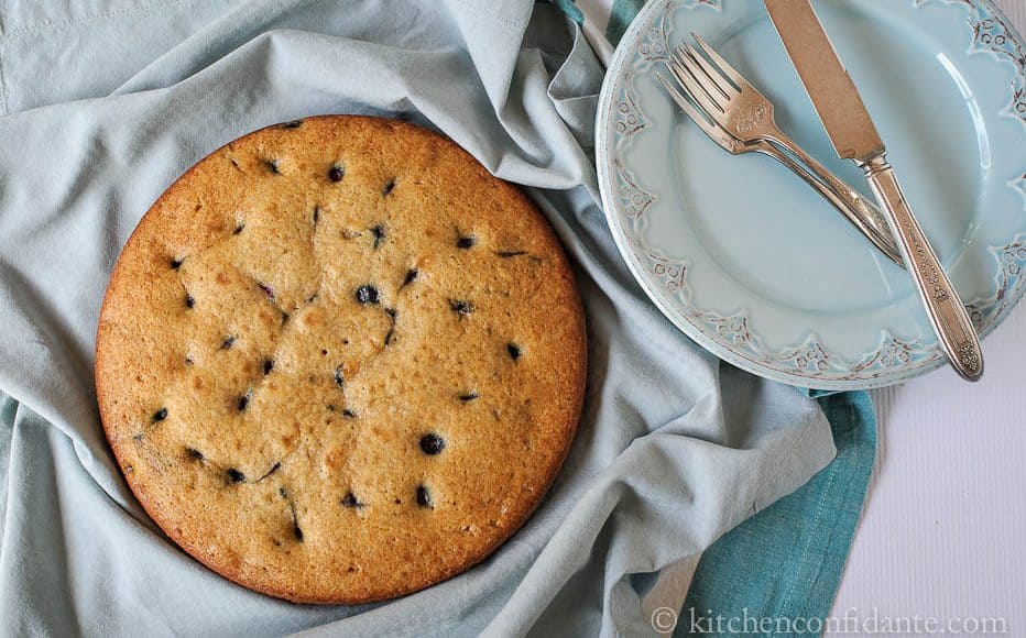 A round blueberry buttermilk cake with plate, fork, and knife.