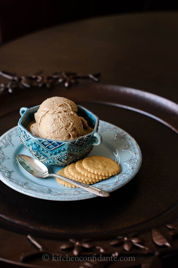 A blue dish of Chai Tea Ice Cream sits on a plate of Coconut Cookies.