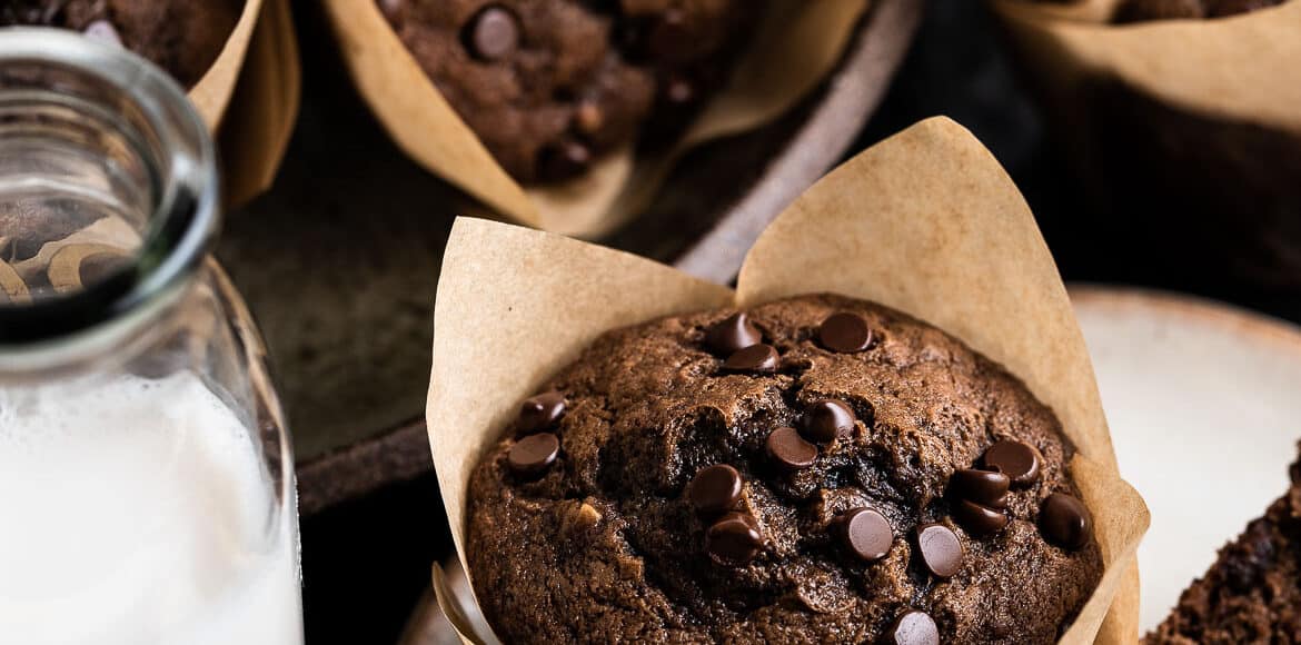 Chocolate banana muffins on a plate with glasses of milk.