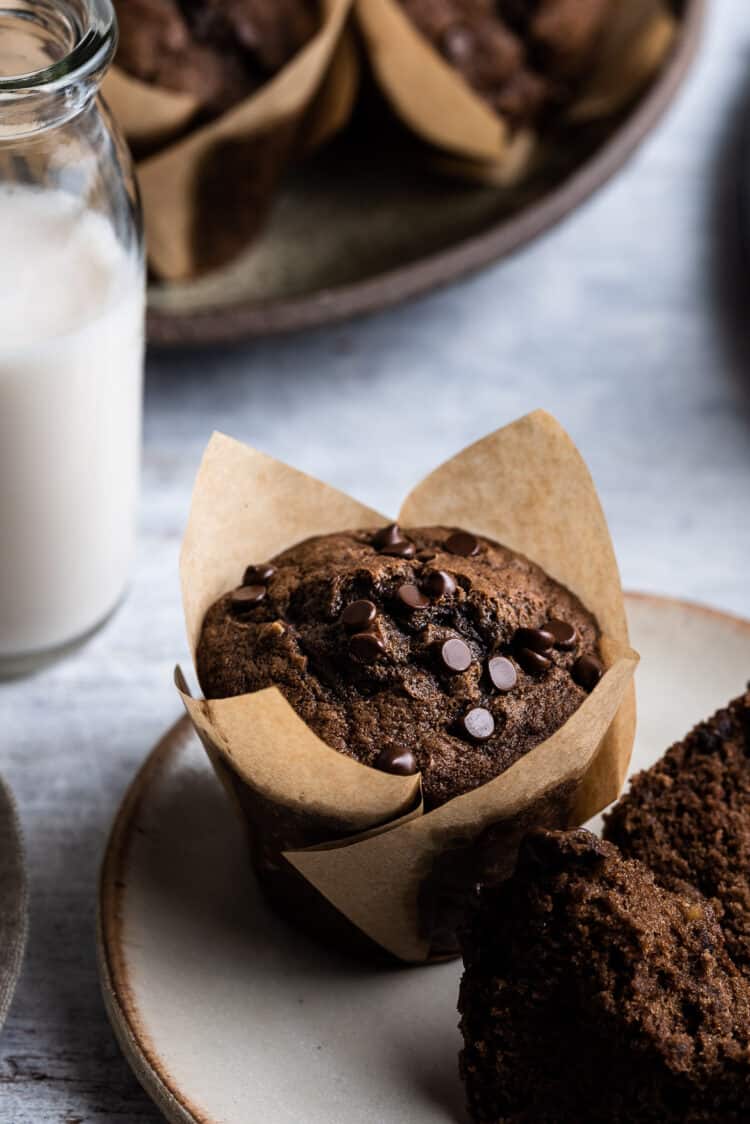 Chocolate banana muffins on a cream plate with glass of milk.