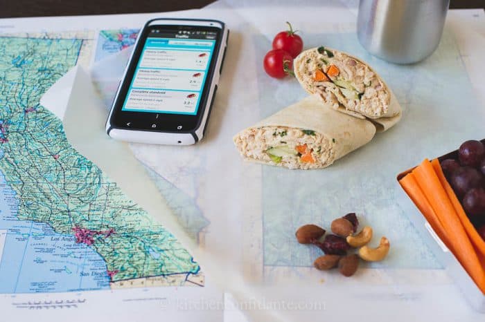 A road map is open to California. A phone sits on the  map, and a lunch is laid out on a piece of wax paper.

