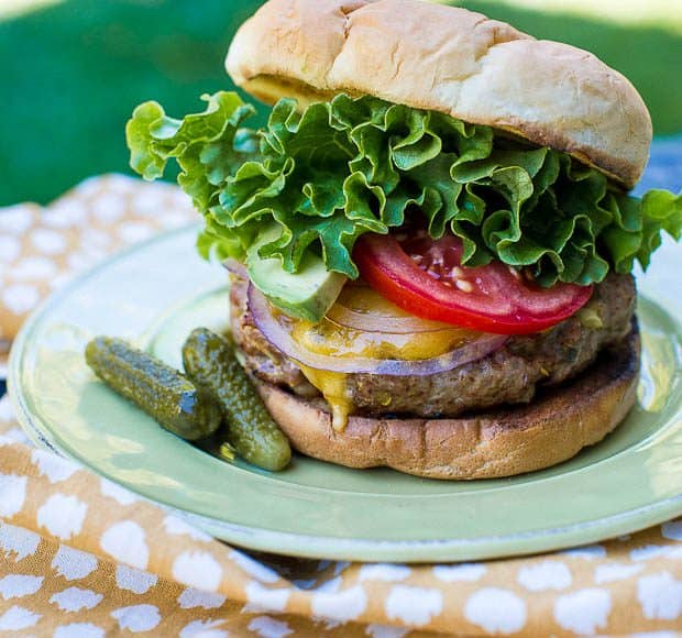 A Southwestern Turkey Burger sits on a green plate. The plate rests on a yellow and white pinic blanket lying on the grass.