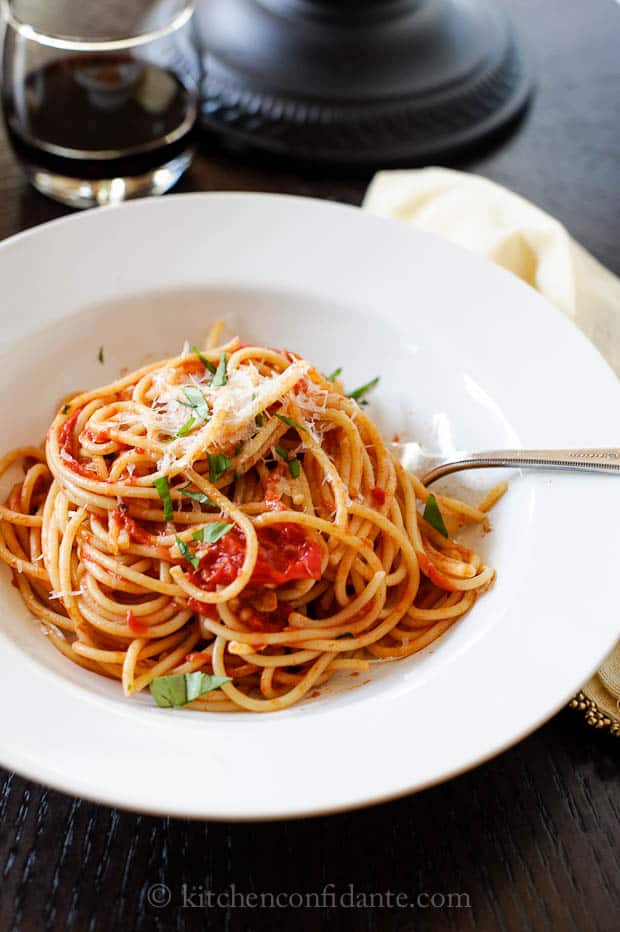 A white bowl filled with spaghetti made with homemade spaghetti sauce topped with fresh basil and parmesean reggiano cheese.