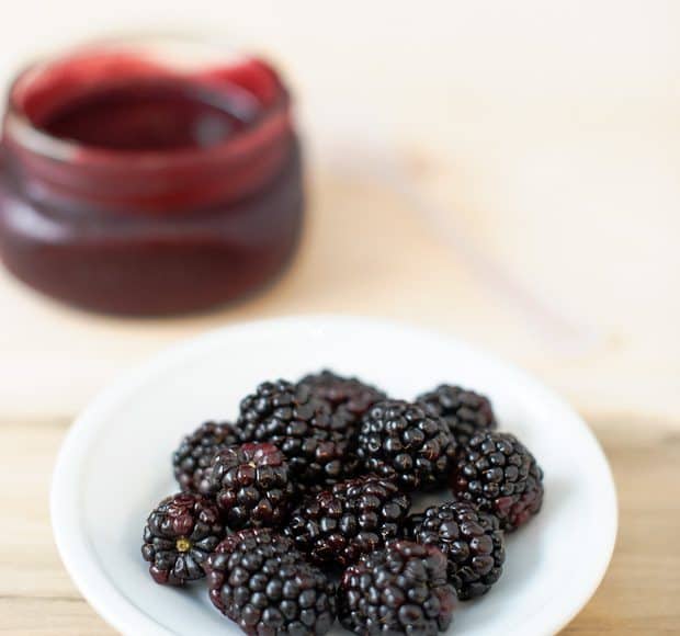 A bowl of fresh blackberries sits in front of a jar of glaze to make blackberry ribs.