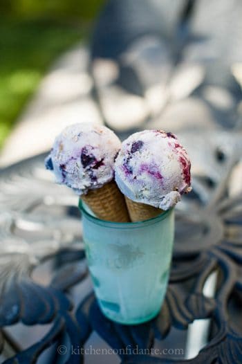 Two sugar cones topped with blueberry crisp ice cream are sitting inside a chilled green jar.