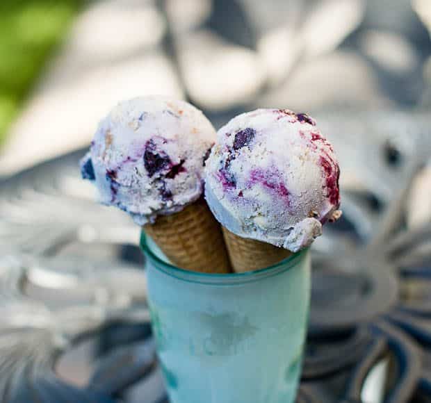 Two sugar cones topped with blueberry crisp ice cream are sitting inside a chilled green jar.