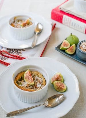 Two dishes of coconut fig clafoutis sit on individual plates, with spoons at the ready, and fresh figs for extra garnish.