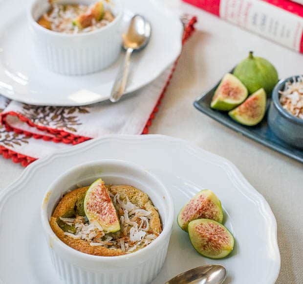 Two dishes of coconut fig clafoutis sit on individual plates, with spoons at the ready, and fresh figs for extra garnish.