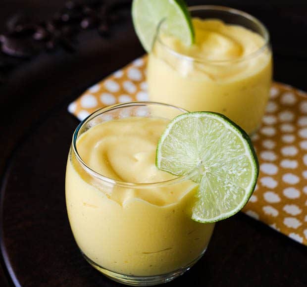 Two glasses full of Mango Coconut Smoothie topped with thin slices of lime.