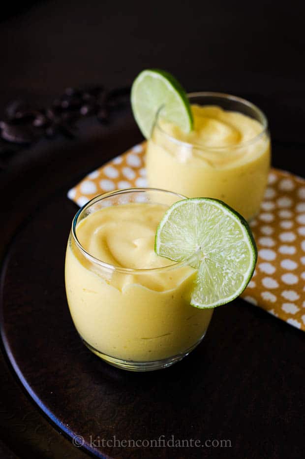 Two glasses full of Mango Coconut Smoothie topped with thin slices of lime.