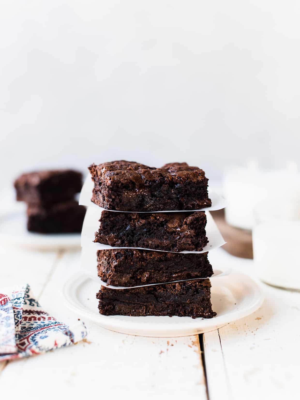 Stack of gooey homemade brownies on a white plate with glasses of milk.