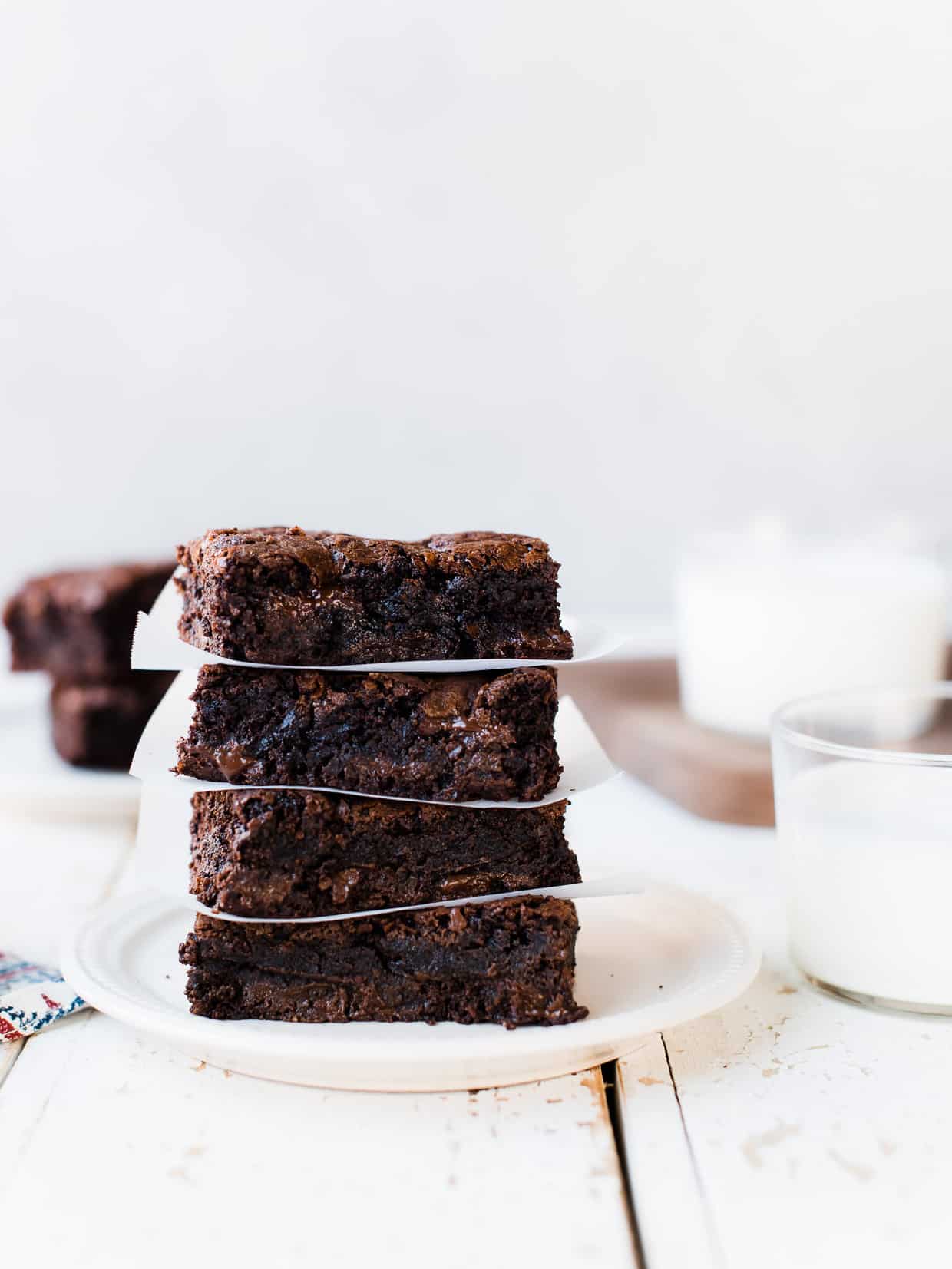 Stack of decadent homemade brownies on a plate, with parchment paper.