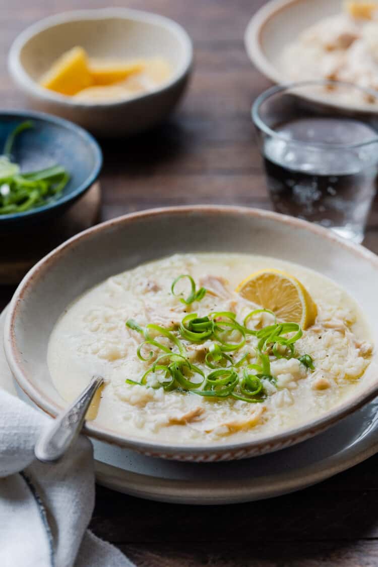 A bowl of Arroz caldo with garnishes of scallions and lemon sitting on a wood table.