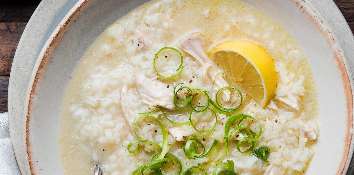 A bowl of Arroz Caldo, Filipino chicken and rice soup, topped with green onion and a slice of lemon.